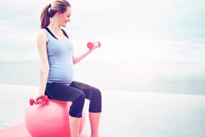 Pregnant woman sitting on ball lifting hand weights